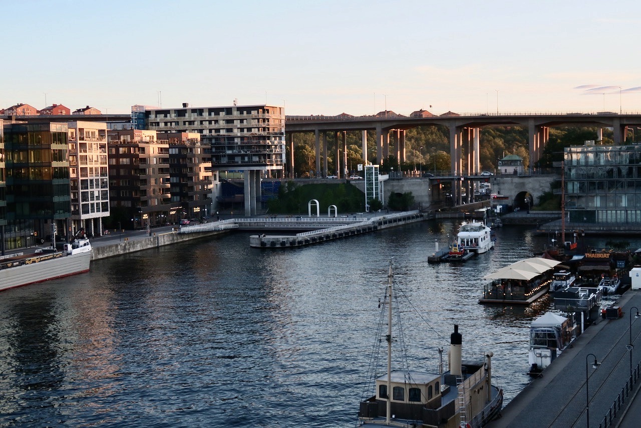 Stockholm. Södermalm. Norra Hammarbyhamnen. Mörkret håller på att sänka sig över kanalen och solen sista strålar lyser under Skanstullsbron och Johanneshovsbron. 